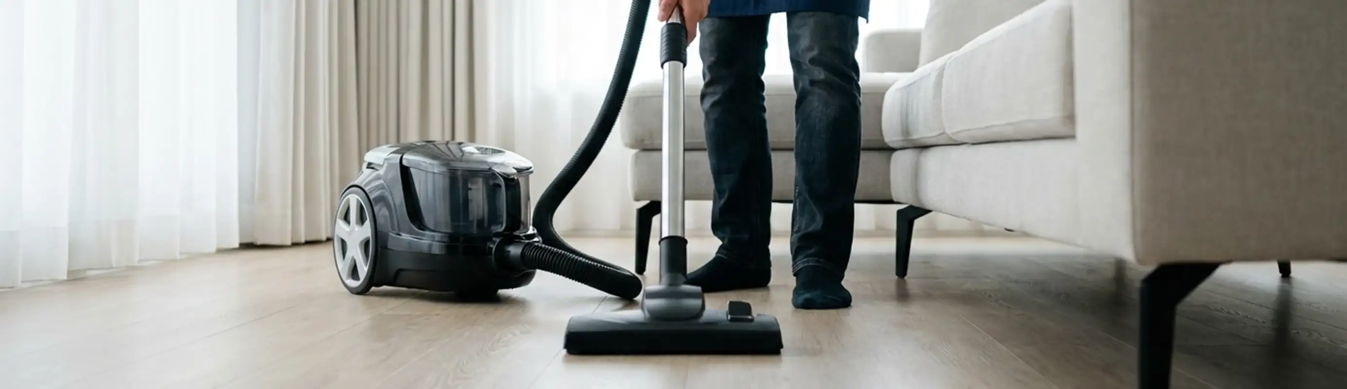 Professional house cleaner vacuuming a living room floor with a canister vacuum cleaner, Fresno, CA.