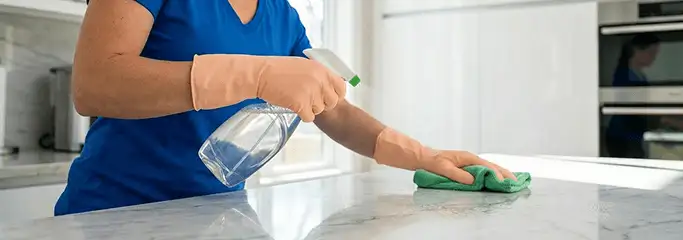 Maid service worker spraying and wiping a kitchen countertop with a microfiber cloth for sanitizing, Fresno, CA.