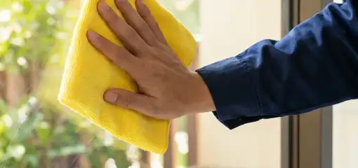 House cleaner wiping a glass window with a yellow microfiber cloth for streak-free cleaning, Fresno, CA.